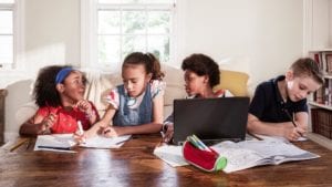 4 kids sitting at a table together working and using a laptop